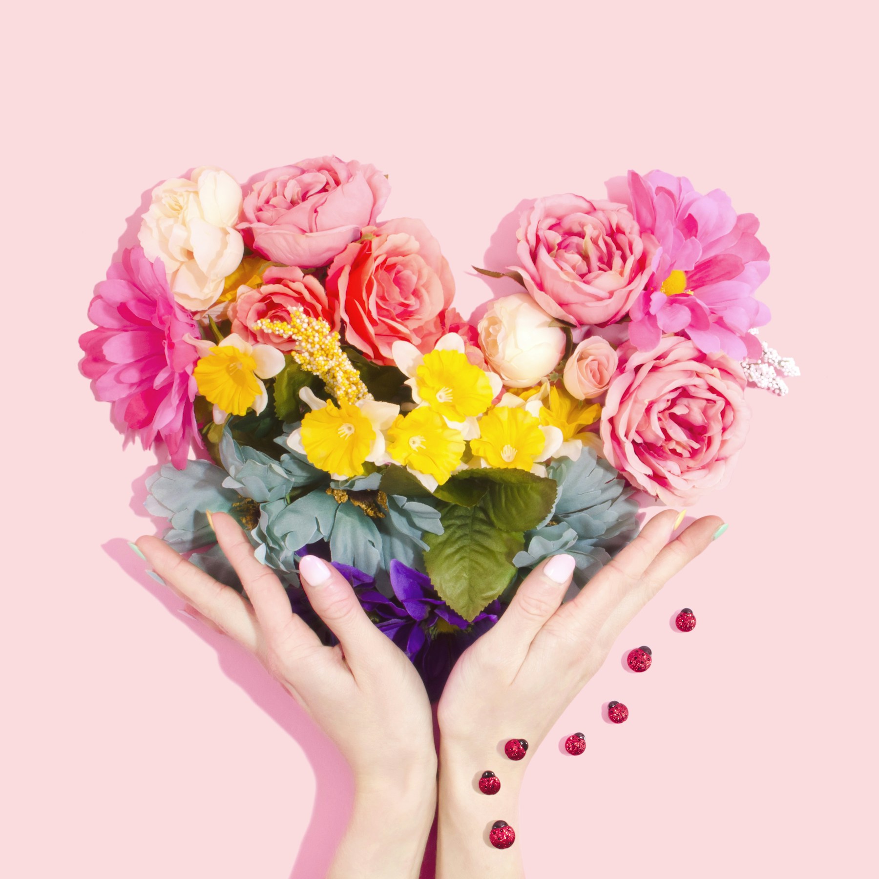 Hands presenting a bright bouquet of pink, cream, and yellow flowers